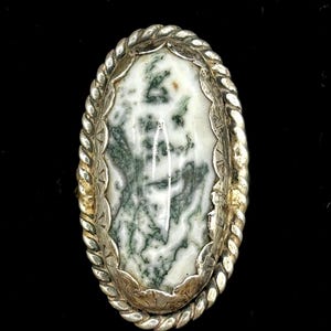 May include: A silver ring with a green and white agate stone set in a rope-like design.