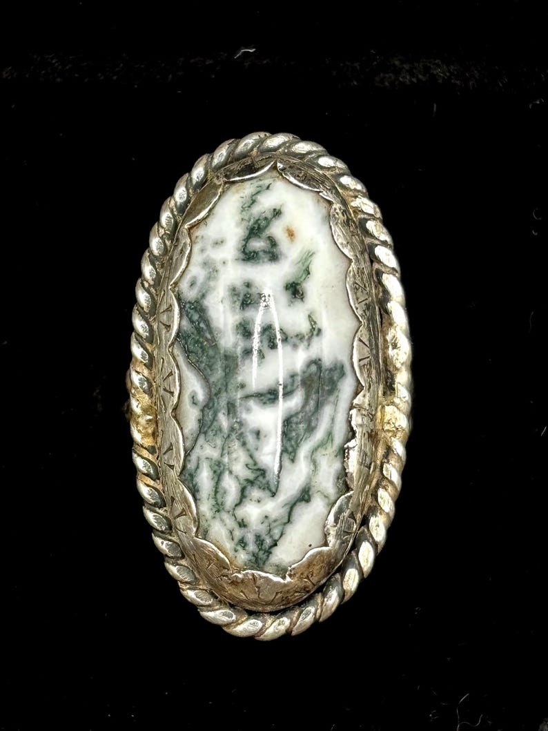 May include: A silver ring with a green and white agate stone set in a rope-like design.