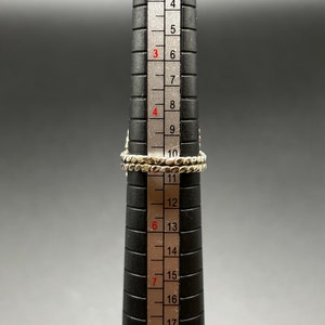 May include: A silver ring with a textured band, measured on a ring sizer, showing a size of 10.5.