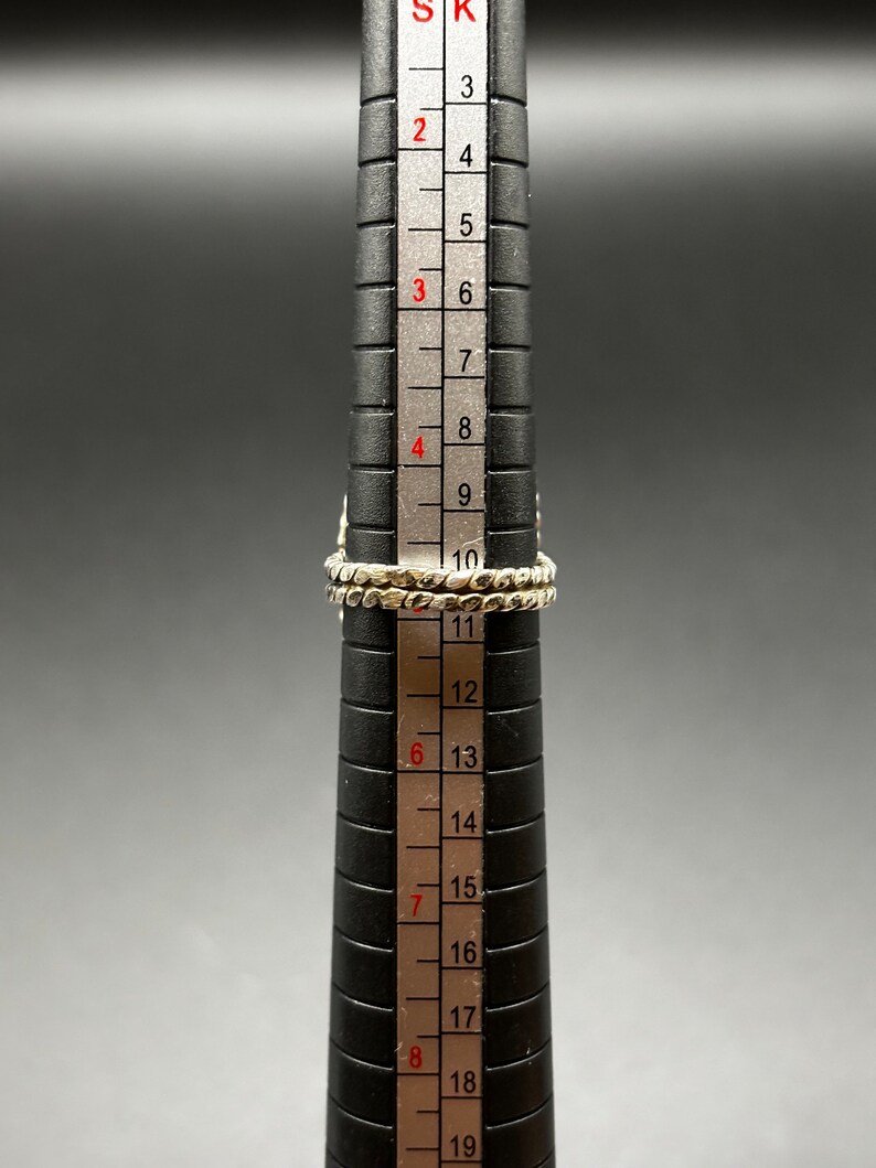 May include: A silver ring with a textured band, measured on a ring sizer, showing a size of 10.5.