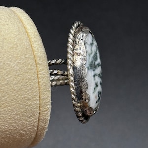 May include: A silver ring with a white and green agate stone. The ring has a rope-like design around the stone.