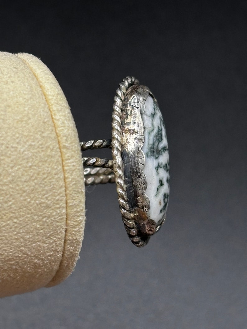 May include: A silver ring with a white and green agate stone. The ring has a rope-like design around the stone.