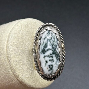 May include: A silver ring with a green and white agate stone set in a rope-like design.