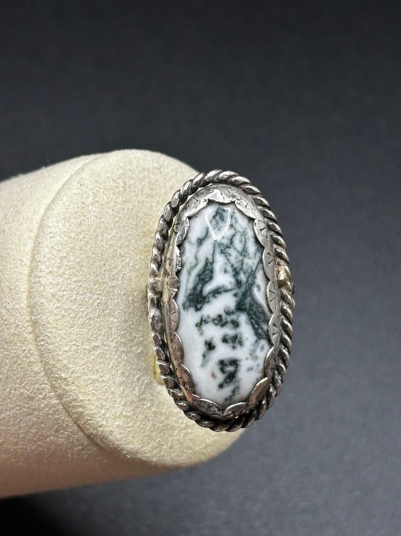 May include: A silver ring with a green and white agate stone set in a rope-like design.