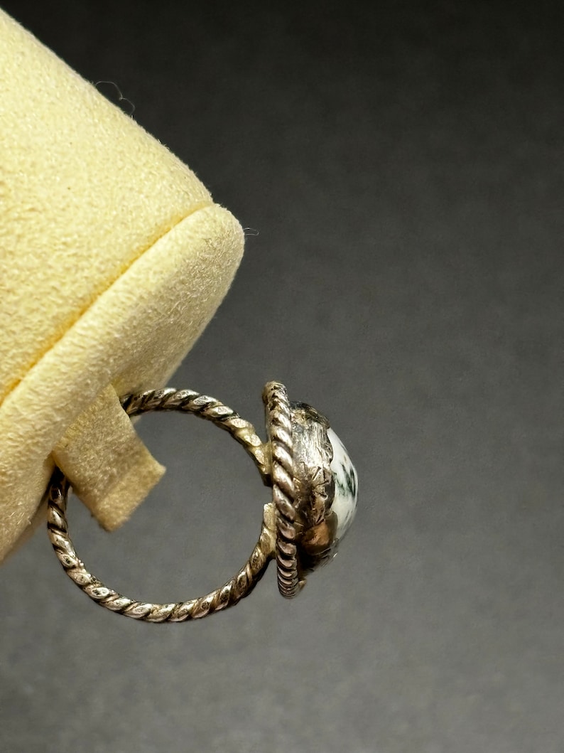 May include: A silver ring with a white and green stone set in a twisted band.