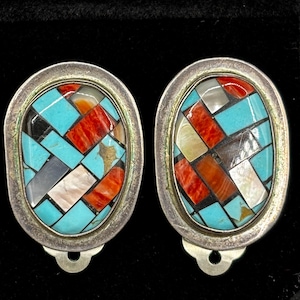 May include: A pair of oval-shaped silver clip-on earrings with a geometric pattern of turquoise, red, white, and black stones.