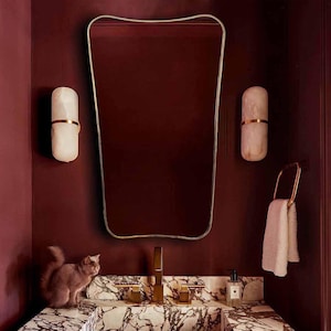 Puede incluir: Un tocador de baño de mármol blanco con un lavabo rectangular y un grifo dorado. El tocador está en una habitación con paredes burdeos y un espejo con marco dorado.