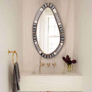 May include: A white ceramic bathroom sink with a gold faucet and a decorative oval mirror with a black and white geometric pattern.