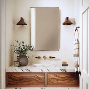 May include: A white marble countertop with a wooden vanity featuring two drawers. The vanity has a white porcelain sink and gold-toned faucets. There is a mirror above the sink with two wall sconces on either side.