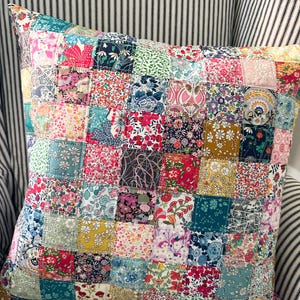 Peut inclure: Un coussin patchwork avec une variété de motifs floraux dans des tons de rose, rouge, bleu, vert et jaune. Le coussin est fait de carrés de tissu cousus ensemble pour créer un design unique et coloré.