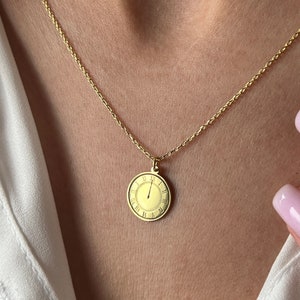 May include: A gold chain necklace with a round clock face pendant. The clock face has Roman numeral markings and a single hand pointing to the 12.