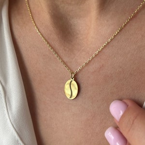 May include: A gold chain necklace with a coffee bean pendant. The pendant is oval shaped and has a detailed outline of a coffee bean.