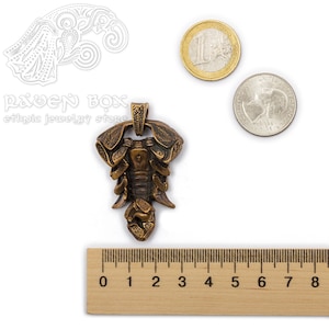Może przedstawiać: Brązowy wisiorek w kształcie skorpiona, o długości około 3 cm. Wisiorek jest ozdobiony misternymi rzeźbami i ma pętelkę na g&oacute;rze do przymocowania łańcuszka.