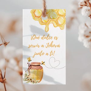 Peut inclure: Une étiquette cadeau rectangulaire avec une illustration à l'aquarelle d'un nid d'abeilles et d'un pot de miel. L'étiquette porte le texte "¡Qué dulce es servir a Jehová junto a ti!" et est suspendue par une ficelle naturelle.
