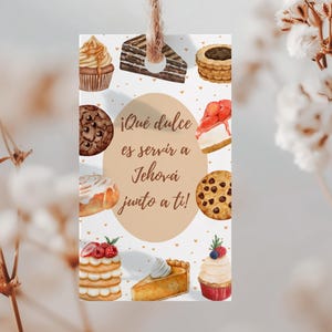 Op de afbeelding: Een rechthoekig label met een touwtje, met aquarel illustraties van verschillende desserts zoals cupcakes, koekjes en stukjes cake. De tekst in het Spaans luidt: "¡Qué dulce es servir a Jehová junto a ti!"