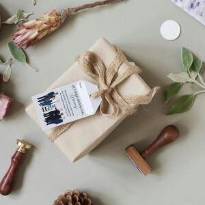 May include: A brown gift box wrapped with twine and a gift tag that reads "Our Wedding Ceremony" and "To our family". The gift tag is decorated with a group of people in blue suits and a yellow and black pattern.