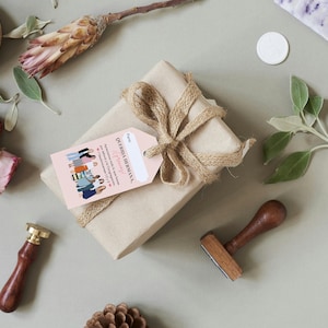 May include: A brown gift box wrapped with twine and a pink gift tag that reads "Our Family is Growing" with a line drawing of a group of women.