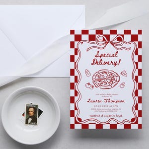 May include: A baby shower invitation with a pizza theme. The invitation features a red and white checkered border and the words "Special Delivery!" in red script. A white envelope, ribbon, and a bowl with a stamp are also in the image.