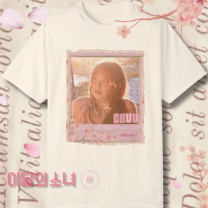 May include: A white t-shirt with a pink and white photo of a woman with the text "CHUU" and "이달의소녀" on it. The photo is surrounded by a pink and white frame.
