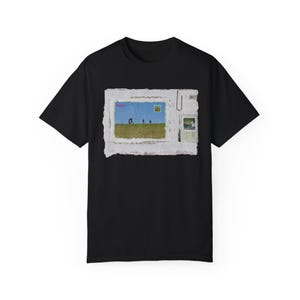 Pode incluir: Camiseta preta com um gr&aacute;fico branco de um cart&atilde;o postal vintage com uma paisagem com quatro figuras caminhando por um campo. O cart&atilde;o postal tem uma borda rasgada e um clipe.