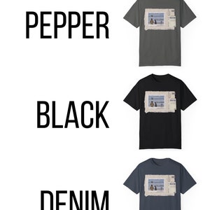 May include: Three t-shirts in different colors: pepper, black, and denim. Each shirt features a graphic print of a vintage postcard with a photo of two people sitting on a bench by the ocean.