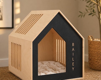 May include: A wooden pet house with a light natural wood finish and a black front panel. The front panel features the name BAILEY in vertical capital letters. The structure has a gabled roof with slats and a soft, tufted off-white cushion inside.