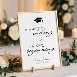 May include: A graduation sign with a gold frame and wooden easel. The sign reads "A sweet ending to a new beginning" with a graduation cap graphic. The sign also includes a name and "Class of 20XX".