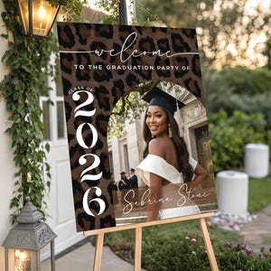 Può includere: Un cartello in legno fatto a mano con la scritta "Welcome" in un carattere giocoso. Il cartello presenta uno sfondo bianco invecchiato e una cornice marrone scuro, perfetto per una porta d'ingresso o un ingresso.