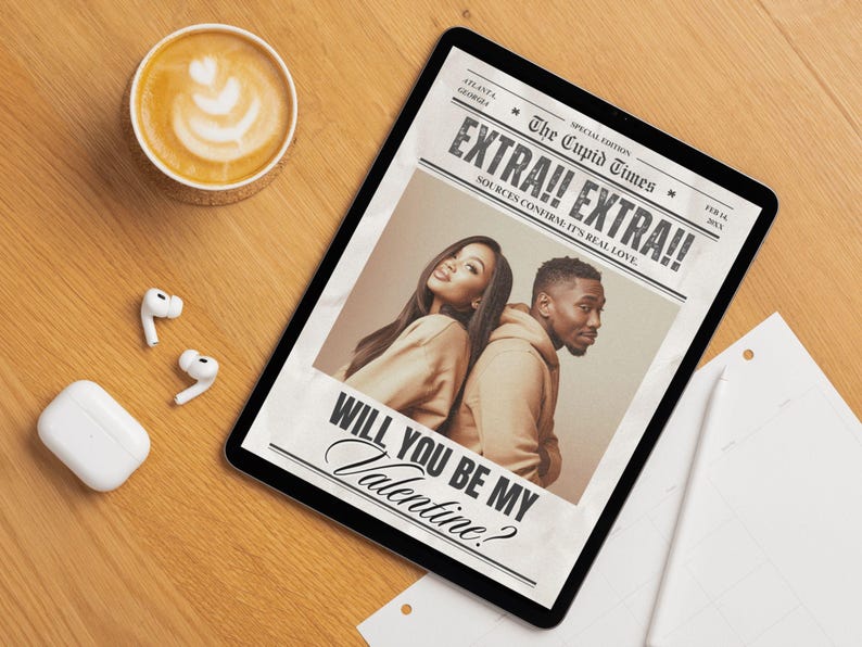 May include: A digital tablet displaying a newspaper-style graphic with the headline "EXTRA!! EXTRA!!" and the text "WILL YOU BE MY Valentine?" A latte and wireless earbuds are on a wooden surface.
