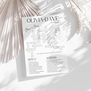 K&ouml;nnte beinhalten: Ein wei&szlig;es Hochzeitskreuzwortr&auml;tsel mit den Namen Olivia und Dave und dem Datum 05.09.202x. Das R&auml;tsel enth&auml;lt Hinweise f&uuml;r die G&auml;ste, um mehr &uuml;ber das Brautpaar zu erfahren. Das Papier liegt auf einer wei&szlig;en Oberfl&auml;che mit Schatten.