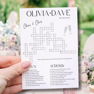 May include: A white card featuring a crossword puzzle titled "Cheers & Clues" for Olivia and Dave's wedding. The date 05.09.202X is displayed. The card includes a crossword and clues, with two champagne glasses drawn at the top.