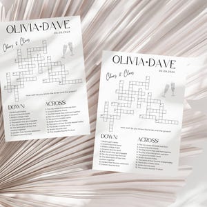 K&ouml;nnte beinhalten: Zwei wei&szlig;e Papierb&ouml;gen mit einem Kreuzwortr&auml;tsel aufgedruckt. Auf der Oberseite jedes Blattes steht "OLIVIA + DAVE" und "Cheers & Clues". Das Datum "05.09.202X" ist ebenfalls oben aufgedruckt. Die Kreuzwortr&auml;tsel sind f&uuml;r eine Hochzeit.