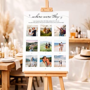May include: A white sign on a wooden easel with the text "where were they" and nine small photos. The sign is for a wedding game, asking guests to guess the locations in the photos.