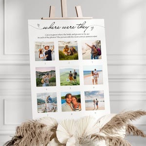 May include: A white sign on an easel with the text "where were they" and nine small photos. The sign is decorated with hearts and asks guests to guess the locations in the photos. The sign is decorated with dried flowers.