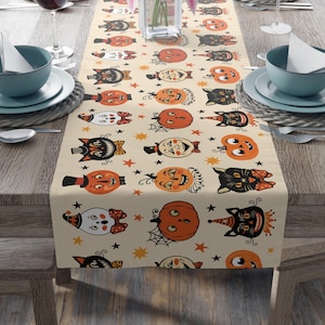 May include: A beige table runner with a repeating pattern of black cats, pumpkins, and stars. The pattern is in a vintage style with a light background and colorful accents.