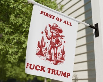 May include: White flag with red text and illustration. The text reads "FIRST OF ALL" and "FUCK TRUMP". The illustration depicts a frog wearing a cowboy hat and boots, giving the middle finger. Cacti are also featured.