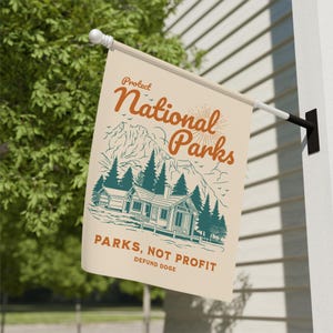 May include: A beige flag with a vintage illustration of a cabin in the woods. The text reads "Protect National Parks, Parks, Not Profit, Defund Doge".