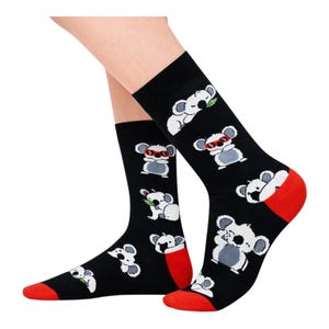 May include: Black socks featuring a repeating pattern of cartoon koalas in different poses, some wearing sunglasses or eating leaves. The toes and heels are red.