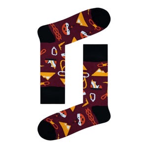 May include: Burgundy socks with black heels and toes, featuring a pattern of climbing equipment. The design includes yellow mountains, white helmets, climbing shoes, and ropes. A fun accessory for outdoor enthusiasts.