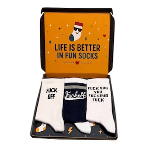 May include: A gift box containing three pairs of socks. The box interior is orange with the text LIFE IS BETTER IN FUN SOCKS. The socks are white and navy blue, featuring black and white text that reads FUCK OFF and FUCK YOU YOU FUCKING FUCK.