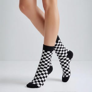 May include: A pair of mid-calf socks featuring a repeating black and white checkerboard pattern. The socks have solid black fabric at the toe and heel sections, providing a distinct contrast to the checkered design that covers the rest of the garment.