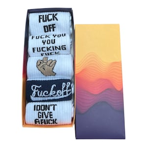 May include: A boxed set of white socks, each printed with bold black text and a middle finger graphic. The socks feature expletive phrases such as "FUCK OFF" and "I DON'T GIVE A FUCK." The box has a decorative, wavy design in shades of orange and purple.