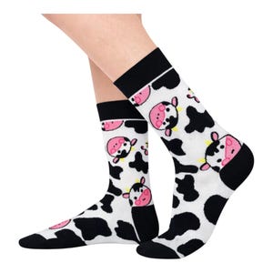May include: White socks with a black top and toe, patterned with black cow spots and pink-faced cow heads. The socks are knee-high and made of a soft material.