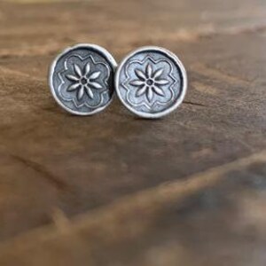 May include: A pair of silver earrings with a floral design. The earrings are round and have a raised flower pattern.