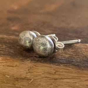 May include: A pair of silver stud earrings with a textured, slightly rough finish. The earrings are round and have a simple, minimalist design.