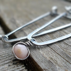 May include: A pair of silver hoop earrings with a pink opal stone on each earring.