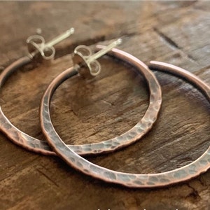 May include: A pair of hammered copper hoop earrings with silver post backs. The earrings are a warm copper color with a slightly oxidized finish.