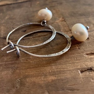 May include: Silver hoop earrings with a hammered finish and a white pearl attached to each hoop.