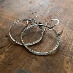 May include: A pair of silver hammered hoop earrings. The earrings are made of a thick gauge wire and have a slightly irregular shape.