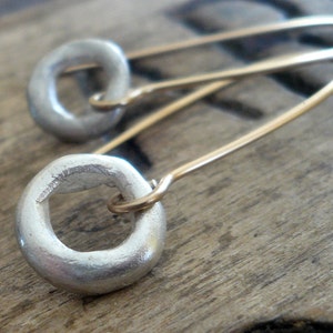 May include: A pair of silver hoop earrings with a simple, rounded design. The earrings are suspended from thin gold wires.